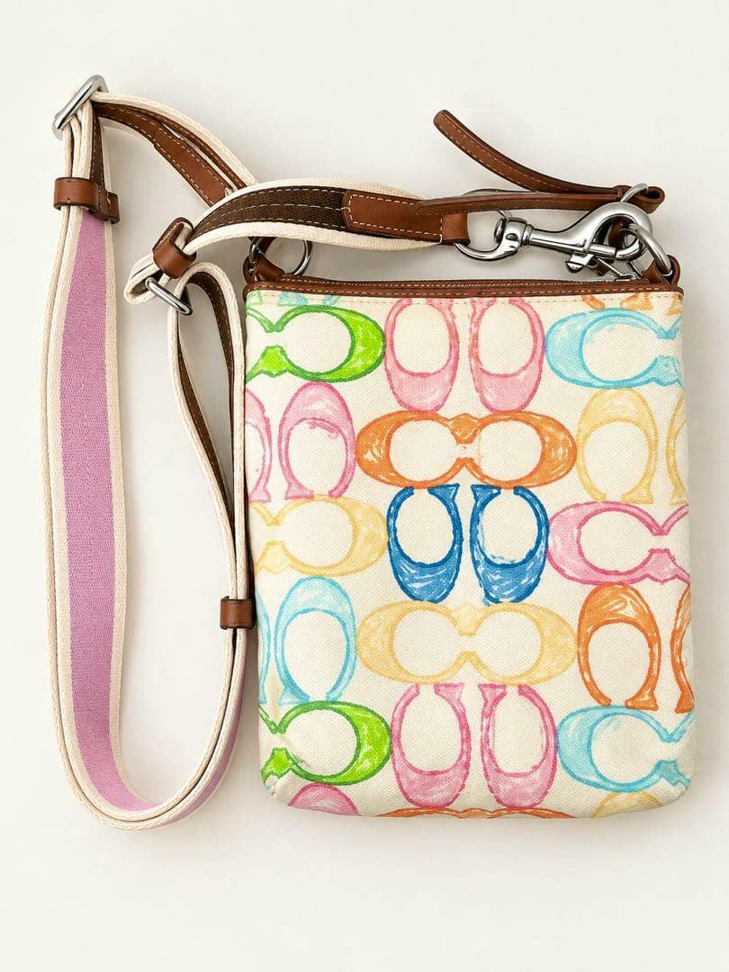 Canvas Coach crossbody bag with multicolor C-pattern print and a shoulder strap with a pink stripe.