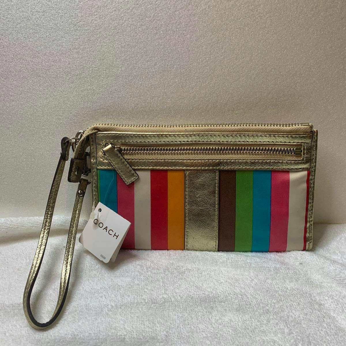 Gold Coach multicolor striped accessory pouch with wrist strap and a Coach tag resting on a white surface.