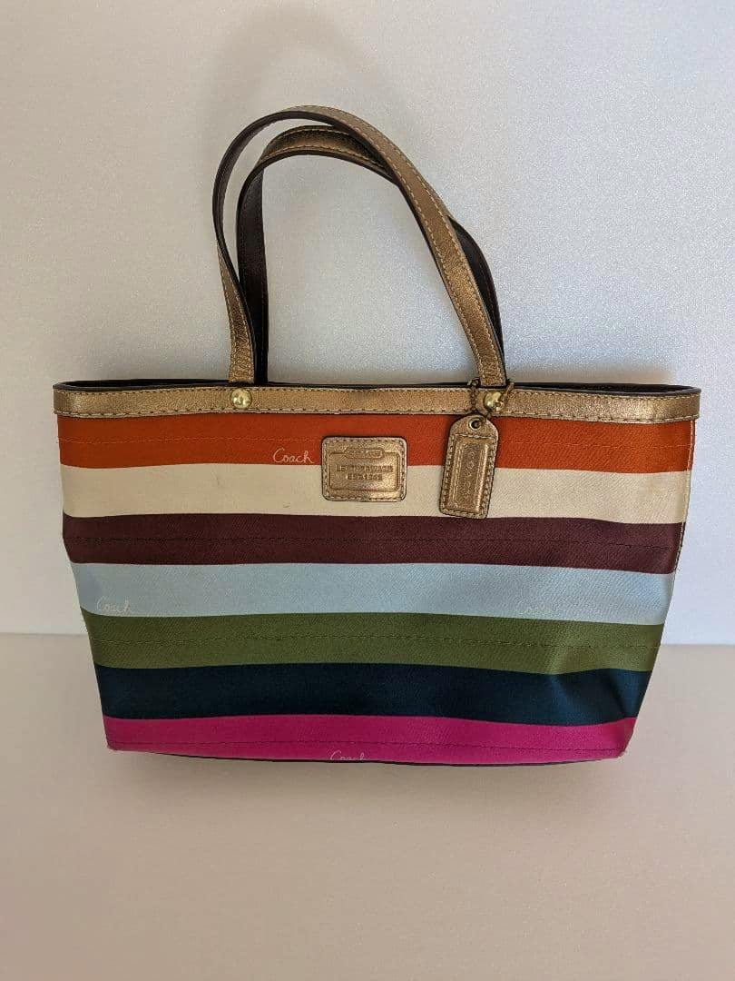Front view of a COACH multicolor striped canvas handbag with gold trim, double handles, and a Coach tag.