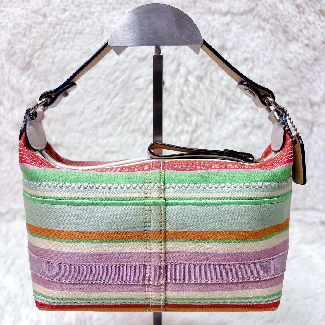 Multicolor striped canvas one-shoulder COACH bag shown on a display stand from the side.