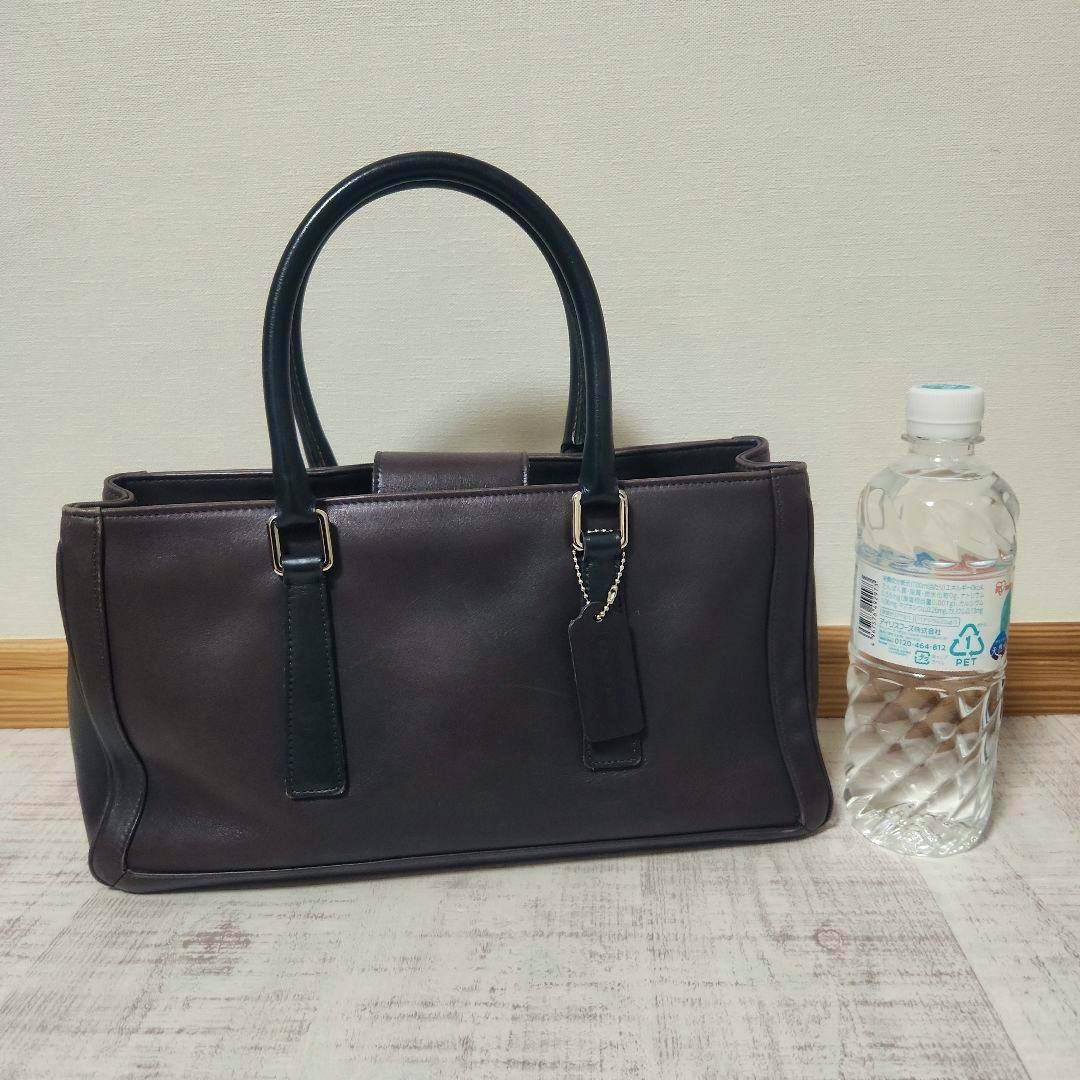 Navy COACH cow leather handbag photographed standing on a floor next to a water bottle for scale.