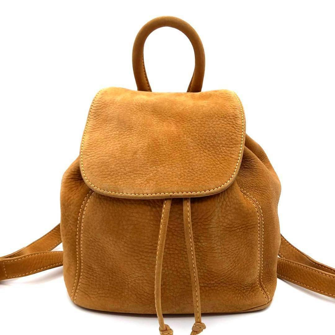 Front view of a tan nubuck backpack with a rounded top handle, flap closure, and drawstring cords.