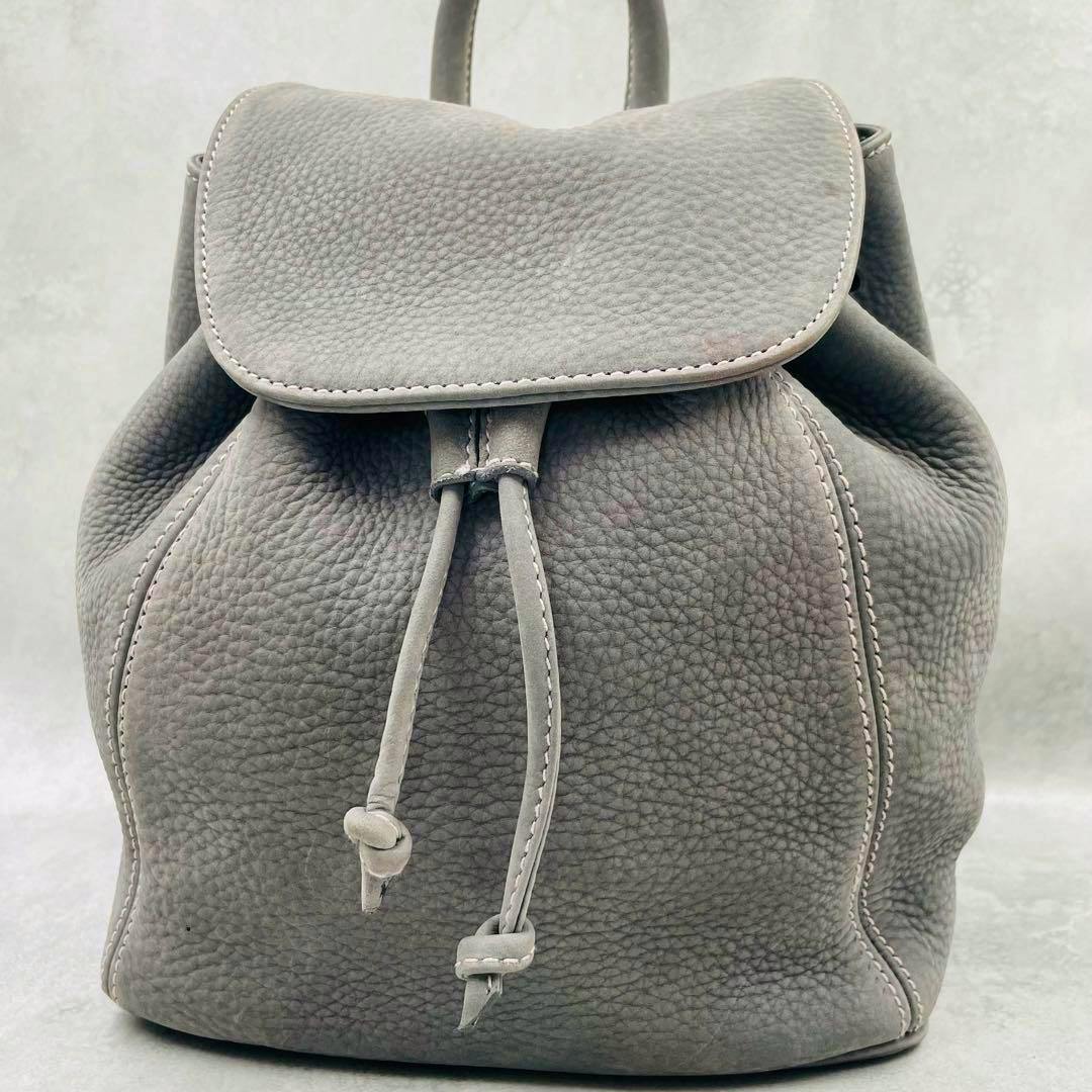 Front view of a gray nubuck leather Coach backpack with a drawstring closure and flap top.