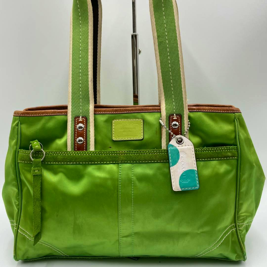 Front-facing green nylon COACH tote bag with striped shoulder straps and a white-and-teal hangtag.