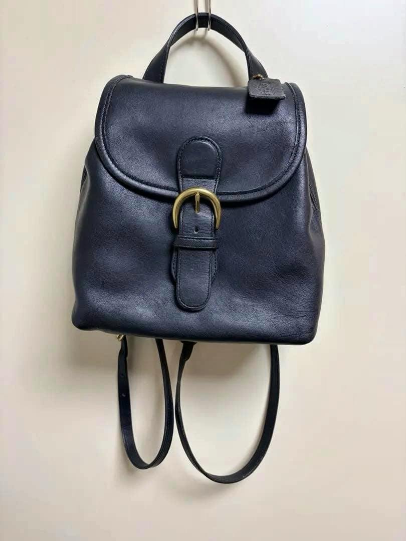 Black Coach cow leather Bantam Bag backpack hanging, showing the front flap and gold buckle.