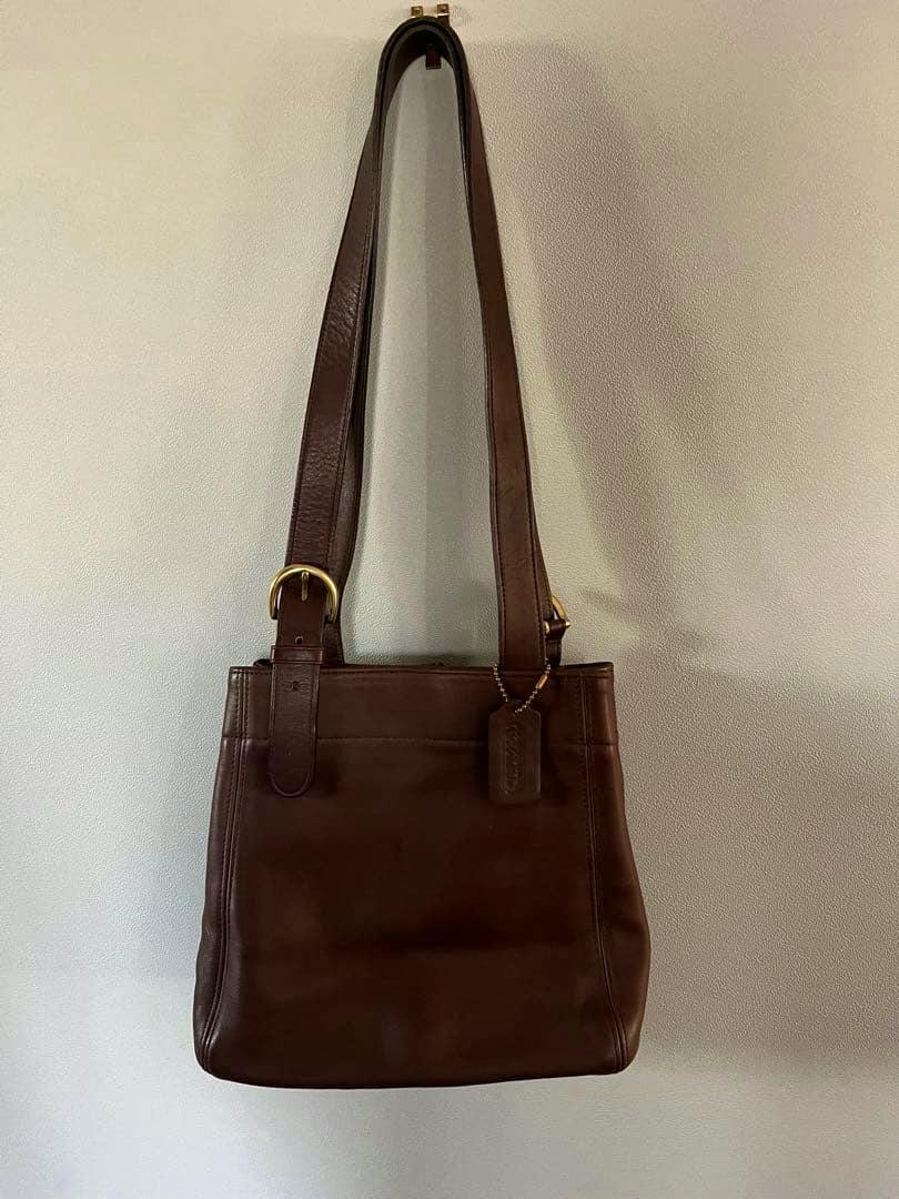 Brown leather COACH shoulder bag (model 4157) hanging on a light wall.