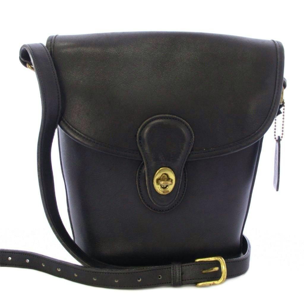 Front view of a black leather Coach bucket-style shoulder bag with a turn-lock closure and adjustable strap.