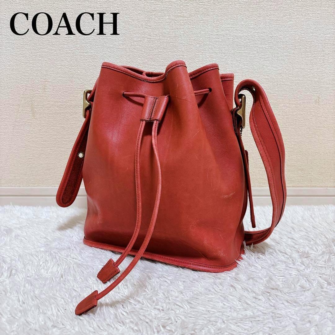 COACH red leather drawstring bucket-style shoulder bag pictured standing on a white rug against a neutral wall.