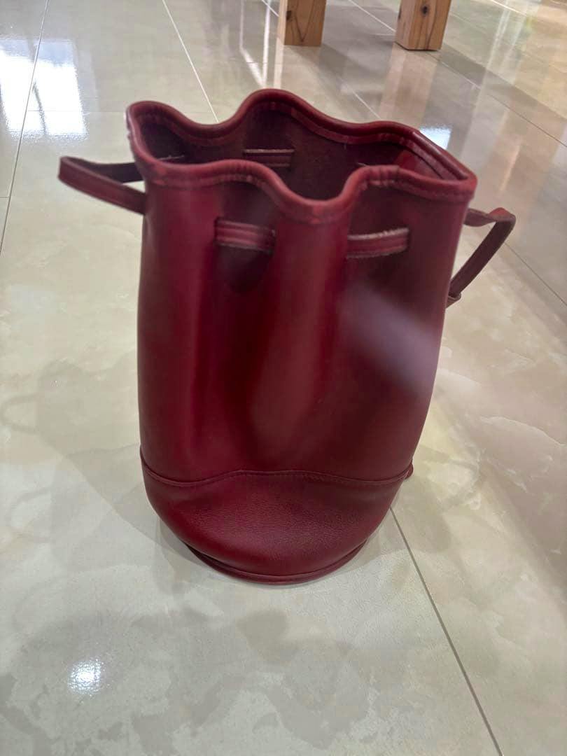 Red COACH drawstring shoulder bag shown upright on a tiled floor with the front and top opening visible.
