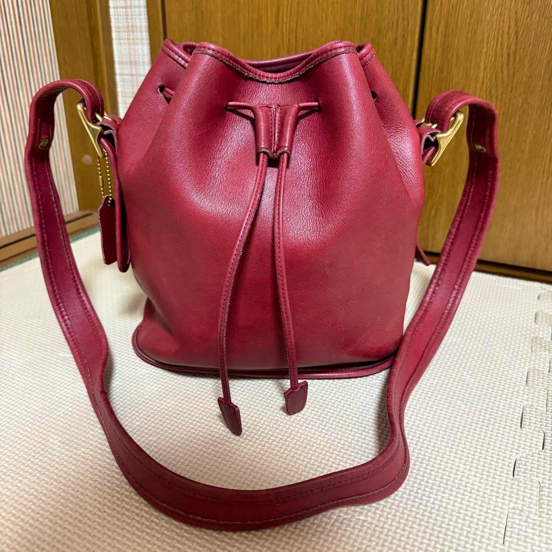 Red COACH cow leather drawstring shoulder bag shown front-facing with its strap visible.