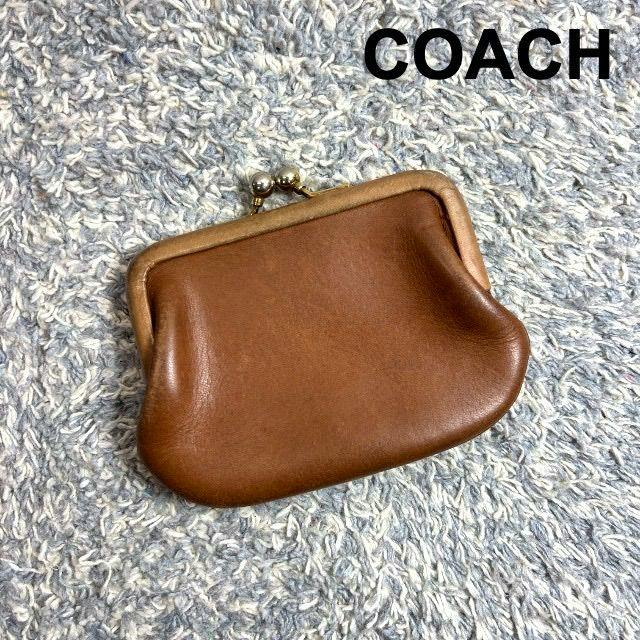 Tan brown COACH leather kiss-lock coin case on a textured gray surface.