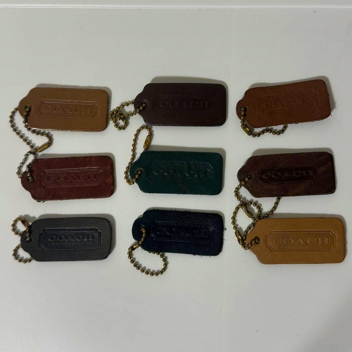 Nine COACH leather bag charms (keychains) in various colors with brass ball chains arranged on a white background.