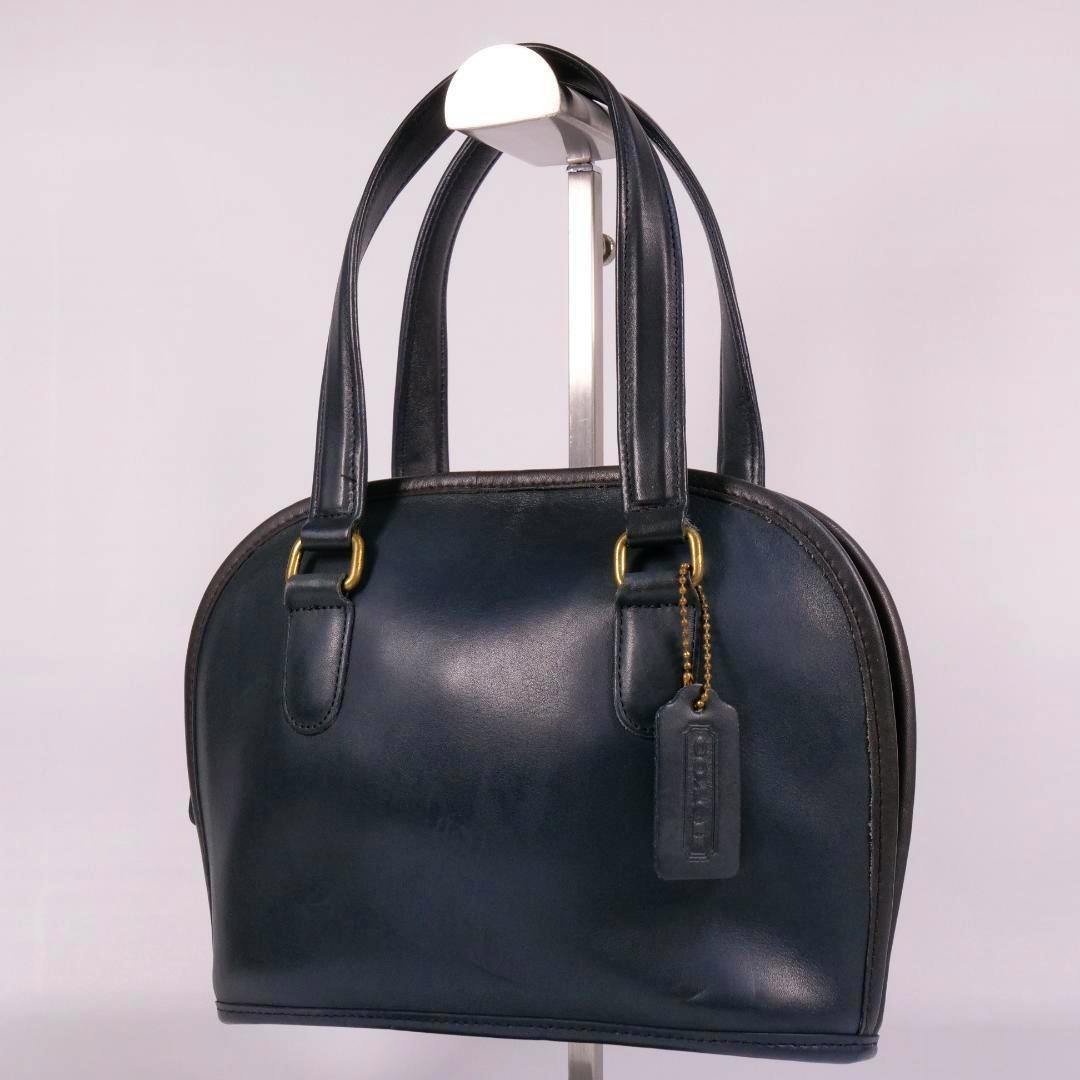 A dark blue leather Coach handbag with double handles and a hanging leather tag displayed on a stand.