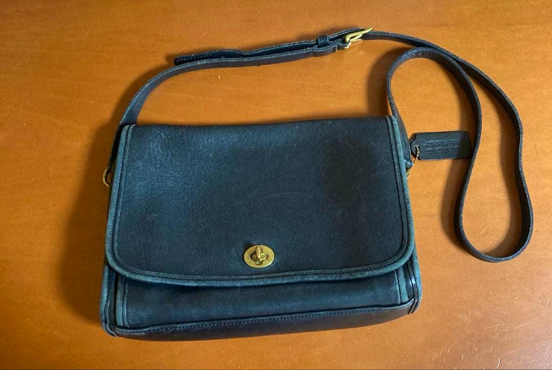 Leather Coach shoulder handbag with flap and turn-lock closure and an adjustable strap lying on a wooden surface.