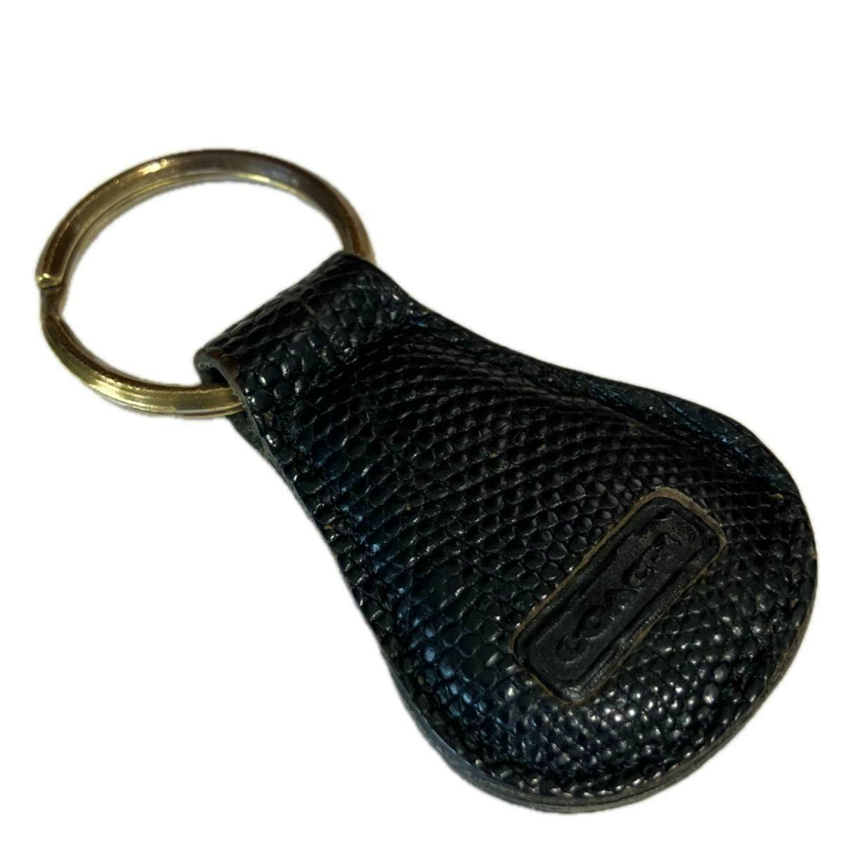 Black leather COACH keychain/key charm with pebble texture, small rectangular logo patch, and gold key ring.
