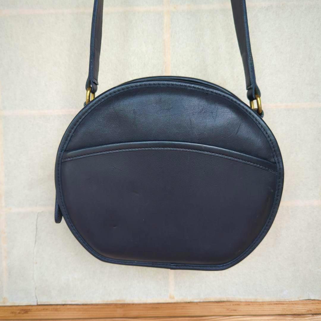 Front view of a round black leather COACH shoulder bag showing an exterior pocket and strap.