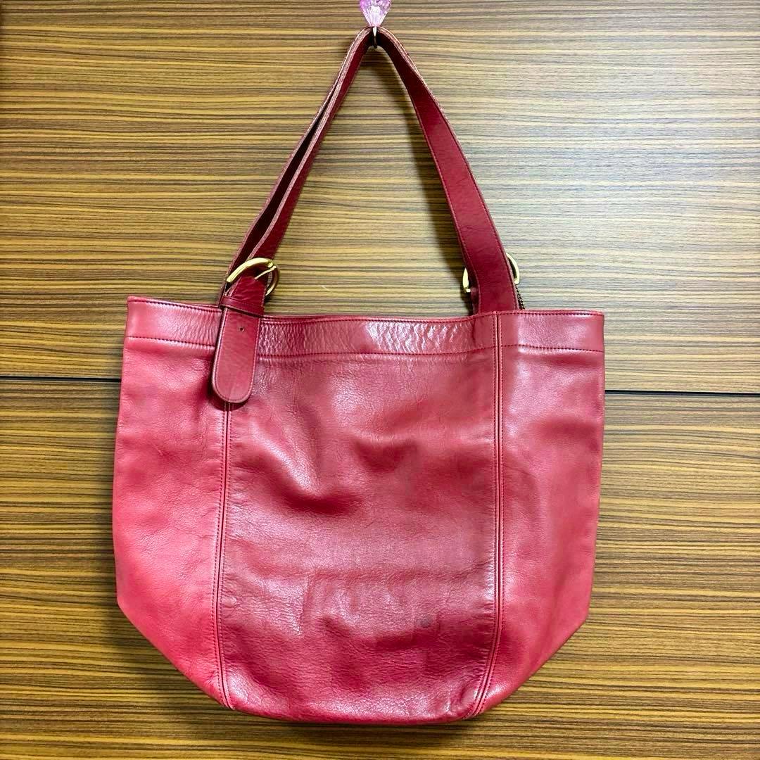 Red leather COACH shoulder bag hanging against a wood-paneled background.