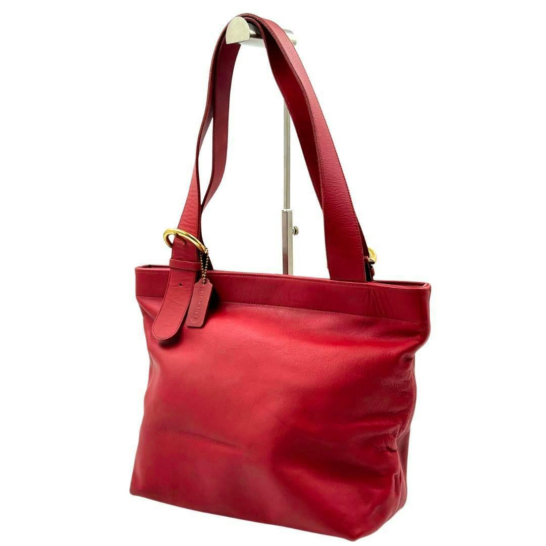 Red COACH leather tote bag displayed on a stand in a three-quarter view.