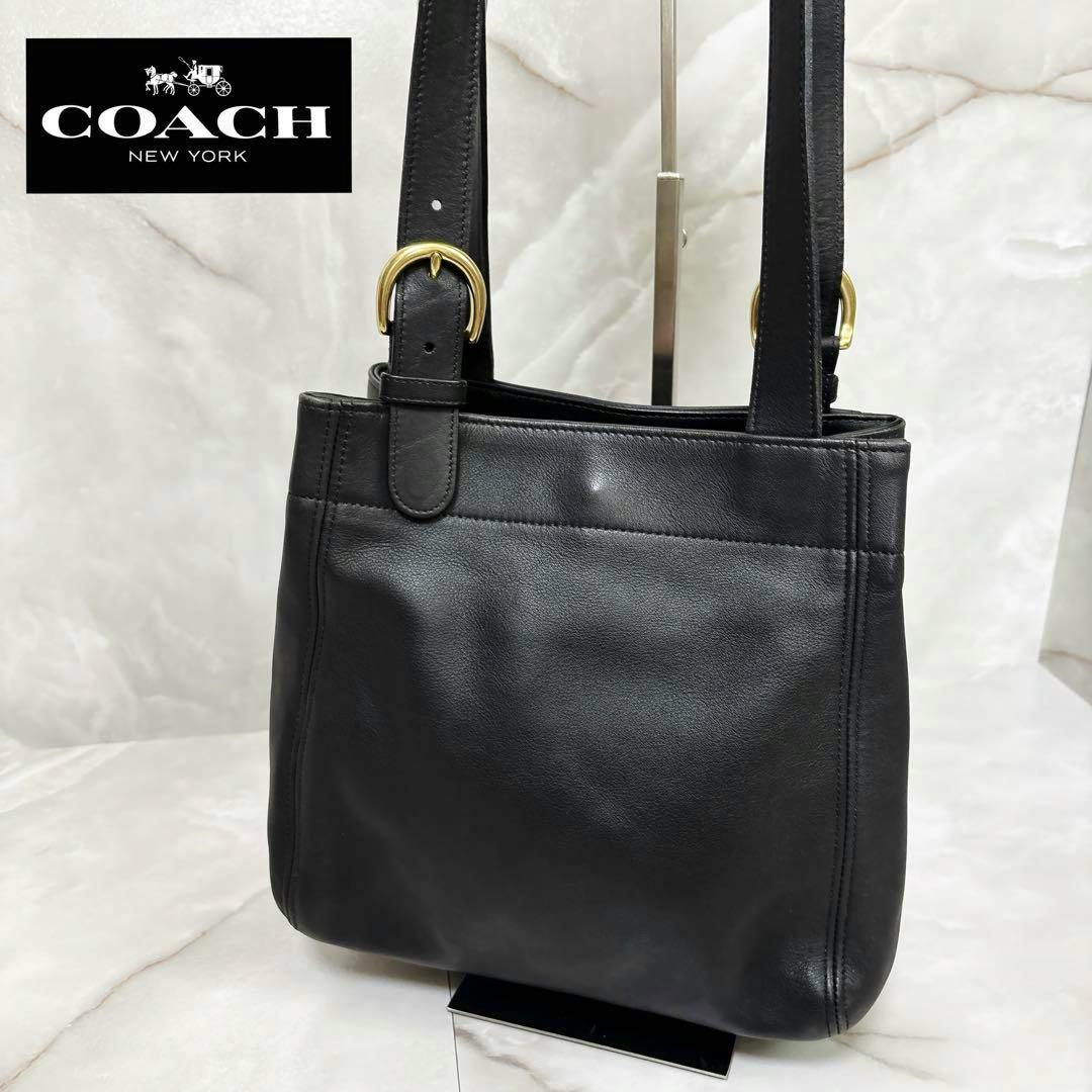 Front view of a black Coach leather tote bag with shoulder straps and gold-tone buckles.