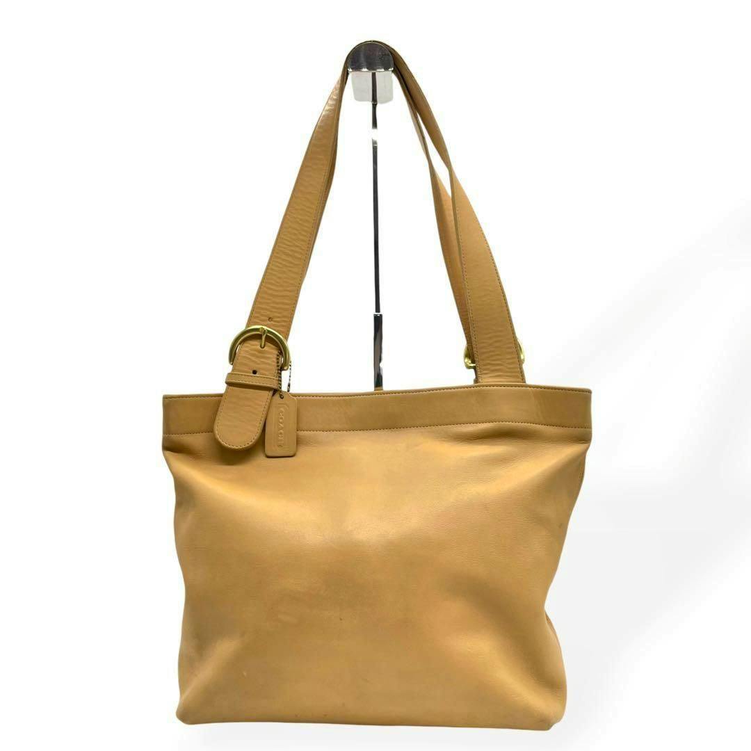 Front view of a yellow-beige leather COACH tote bag with shoulder straps and a small leather tag.