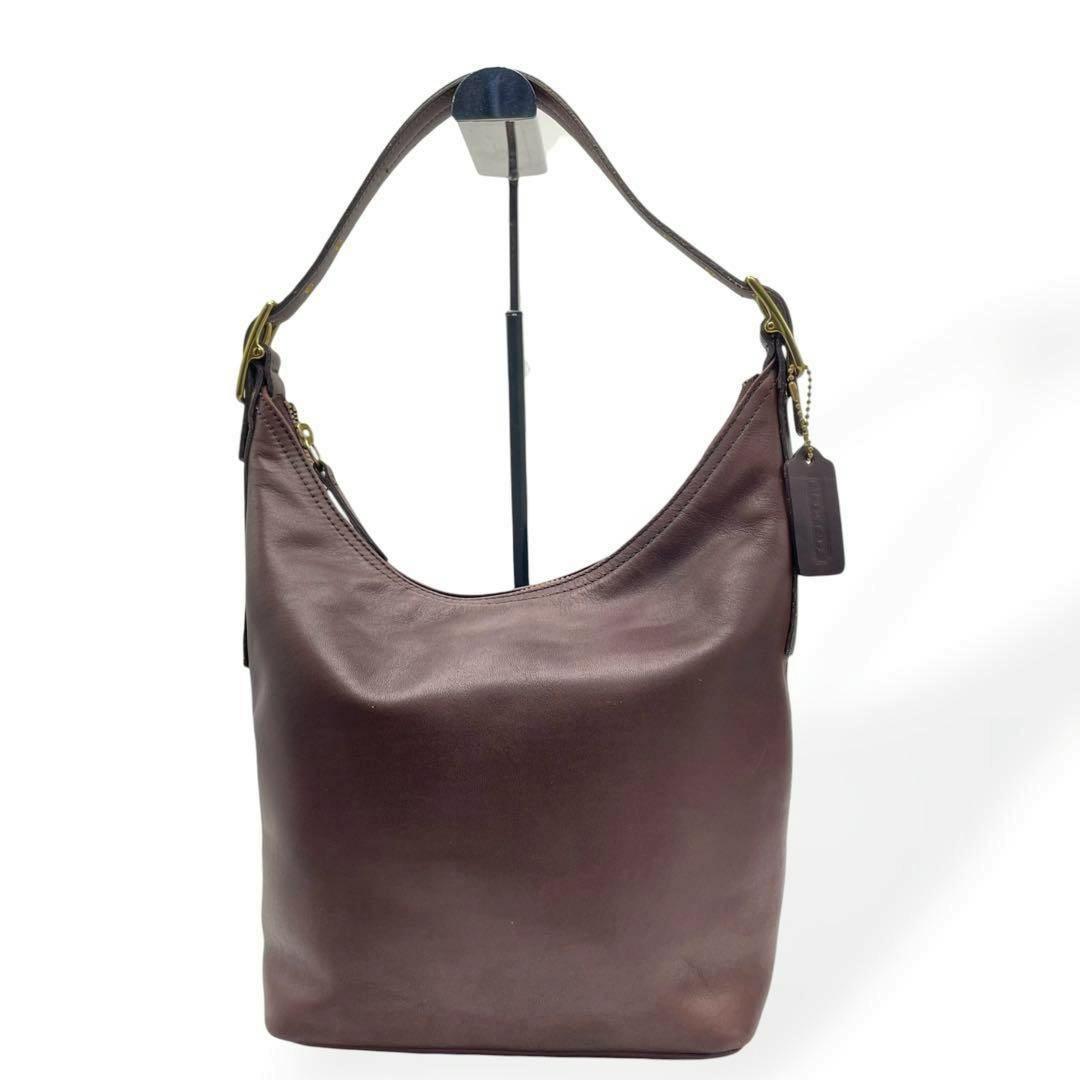 Brown COACH shoulder bag (canvas) shown front-facing hanging on a display stand against a white background.