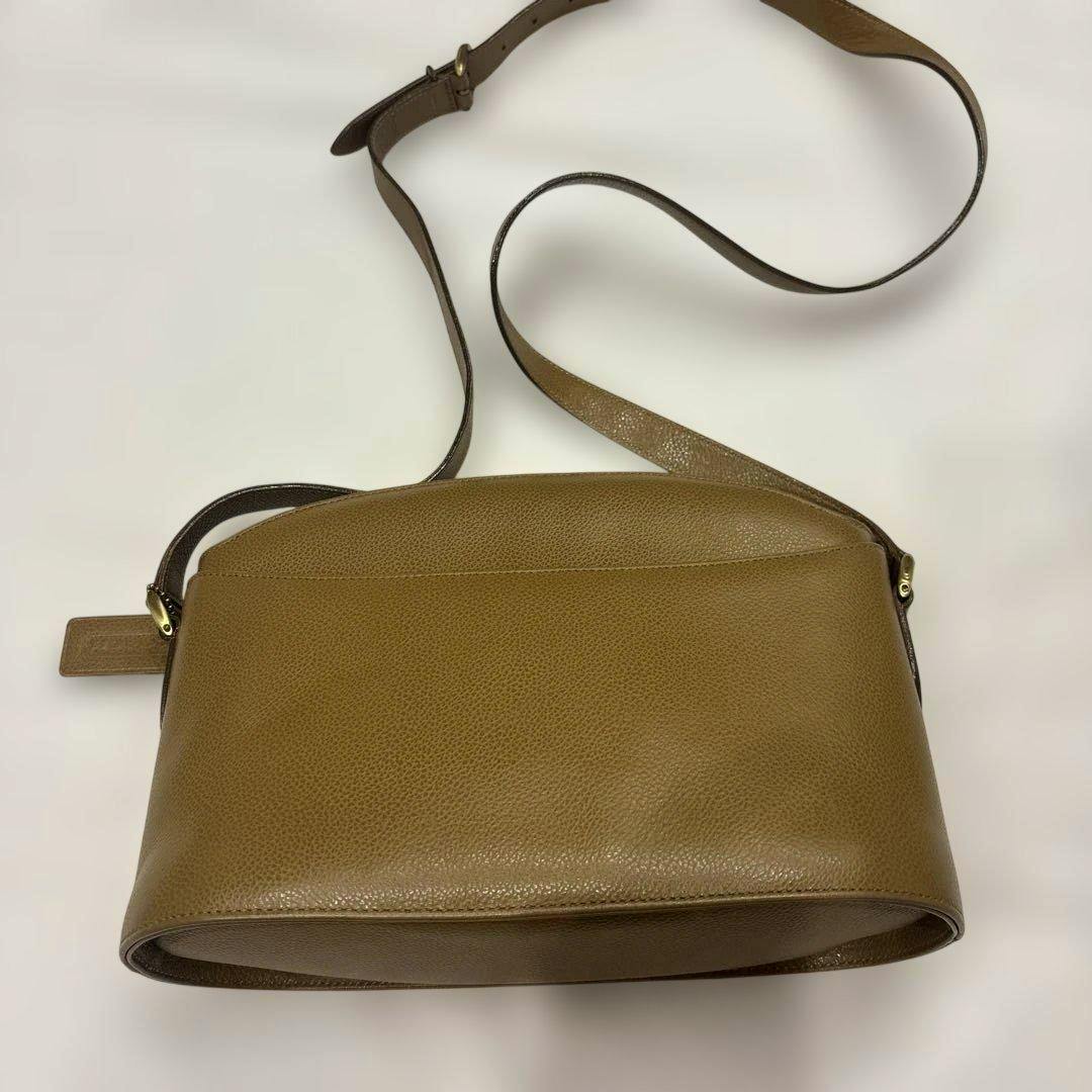 Brown COACH cow leather shoulder bag lying flat with its adjustable strap visible on a white background.
