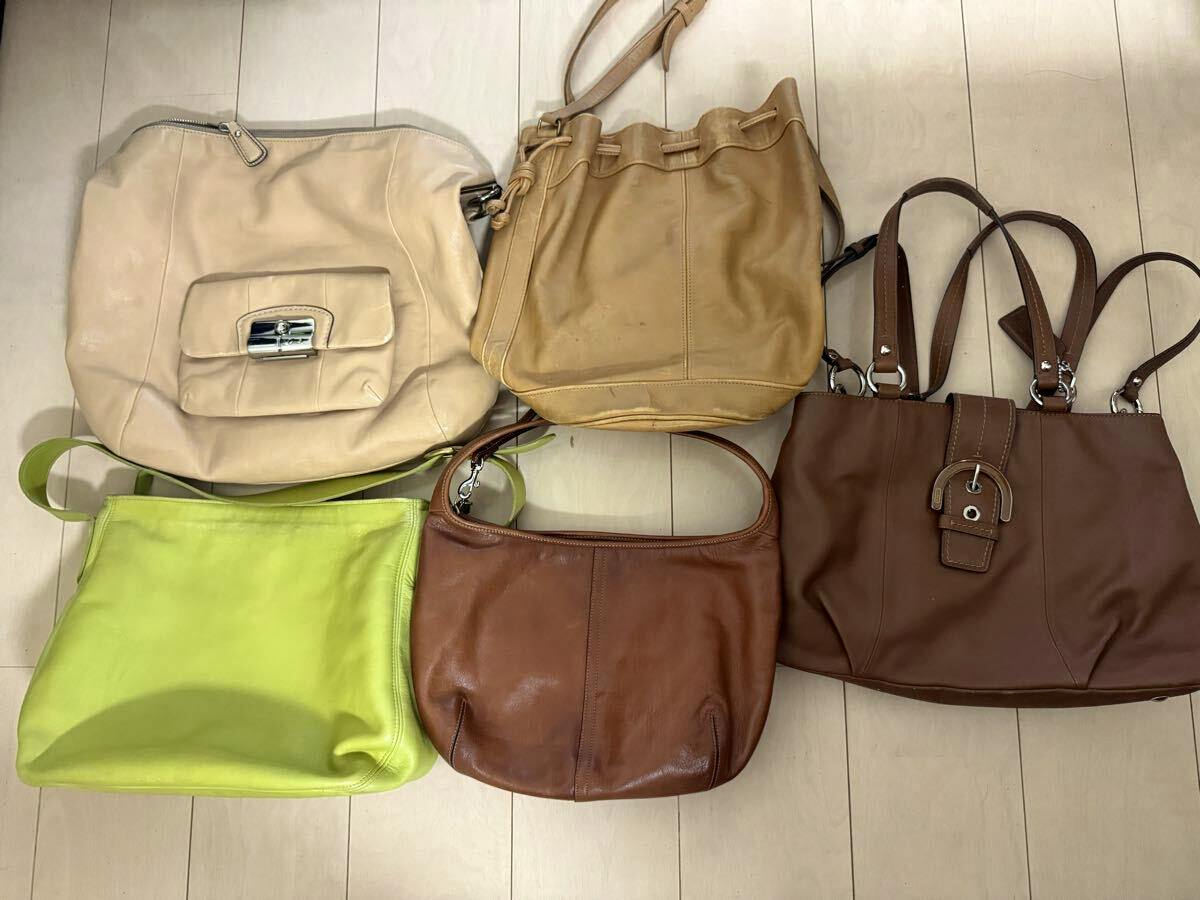 Top-down photo of five COACH bags in different leather colors laid on a light wood floor.