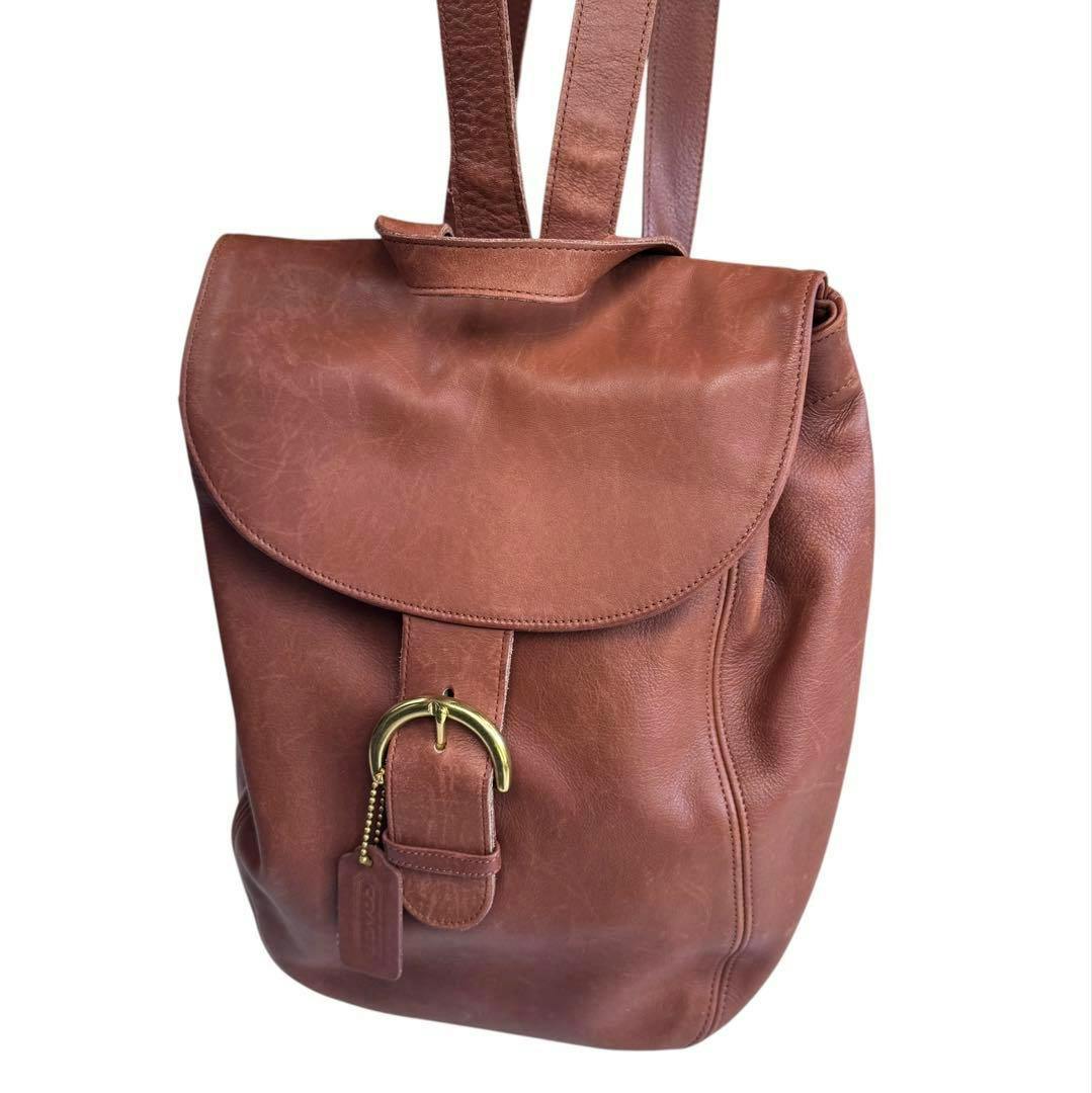 Brown Coach cow leather backpack, front view with flap, brass buckle, and leather tag.