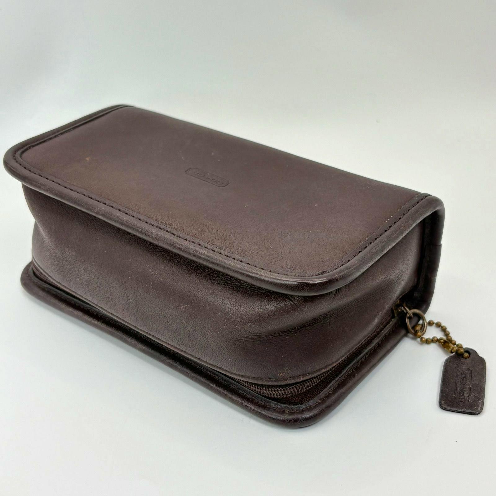 Close-up of a brown leather COACH pouch showing a zipper and a leather tag on a ball chain.