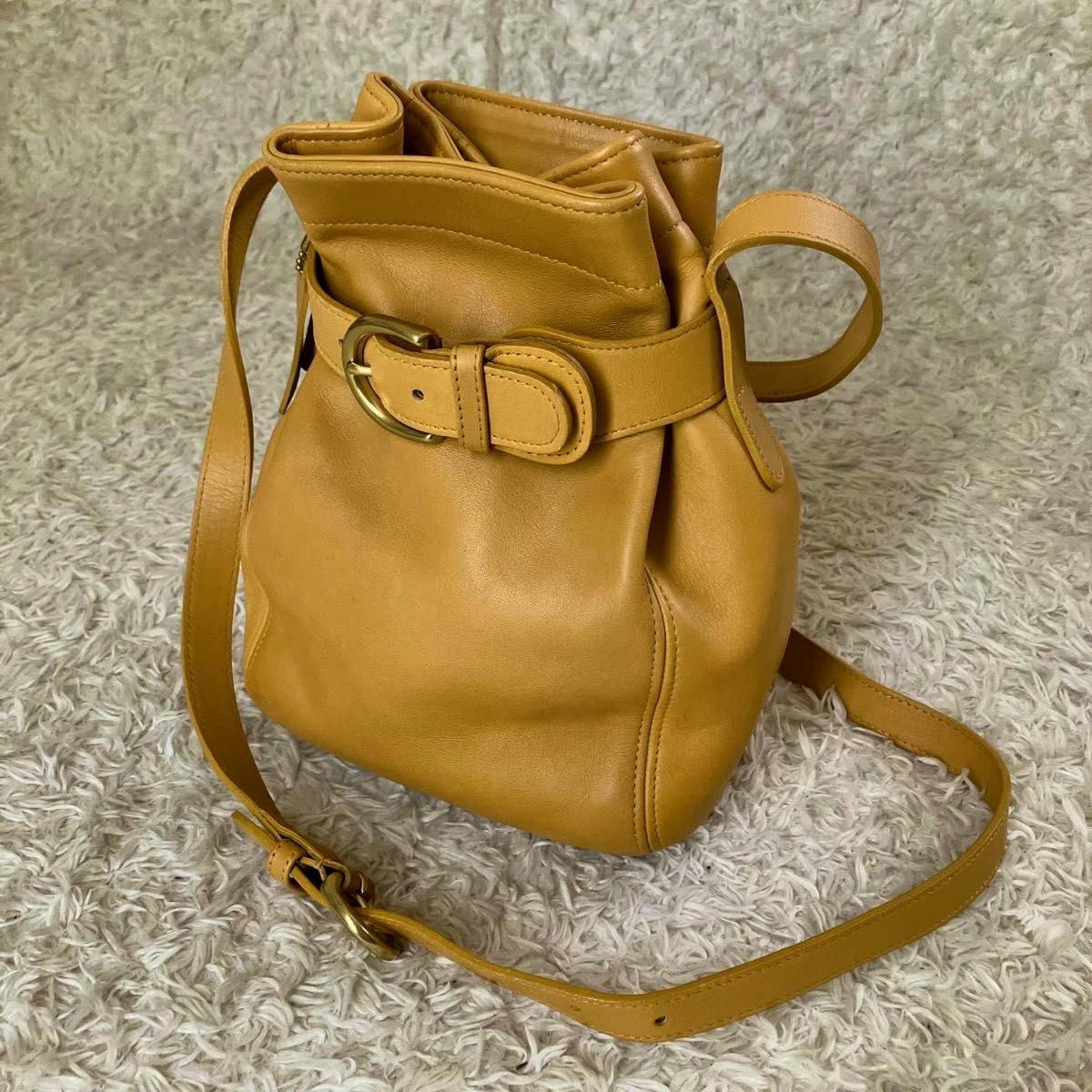 Yellow Coach vintage bucket-style drawstring leather shoulder bag with buckle belt detail photographed on a light shag rug.