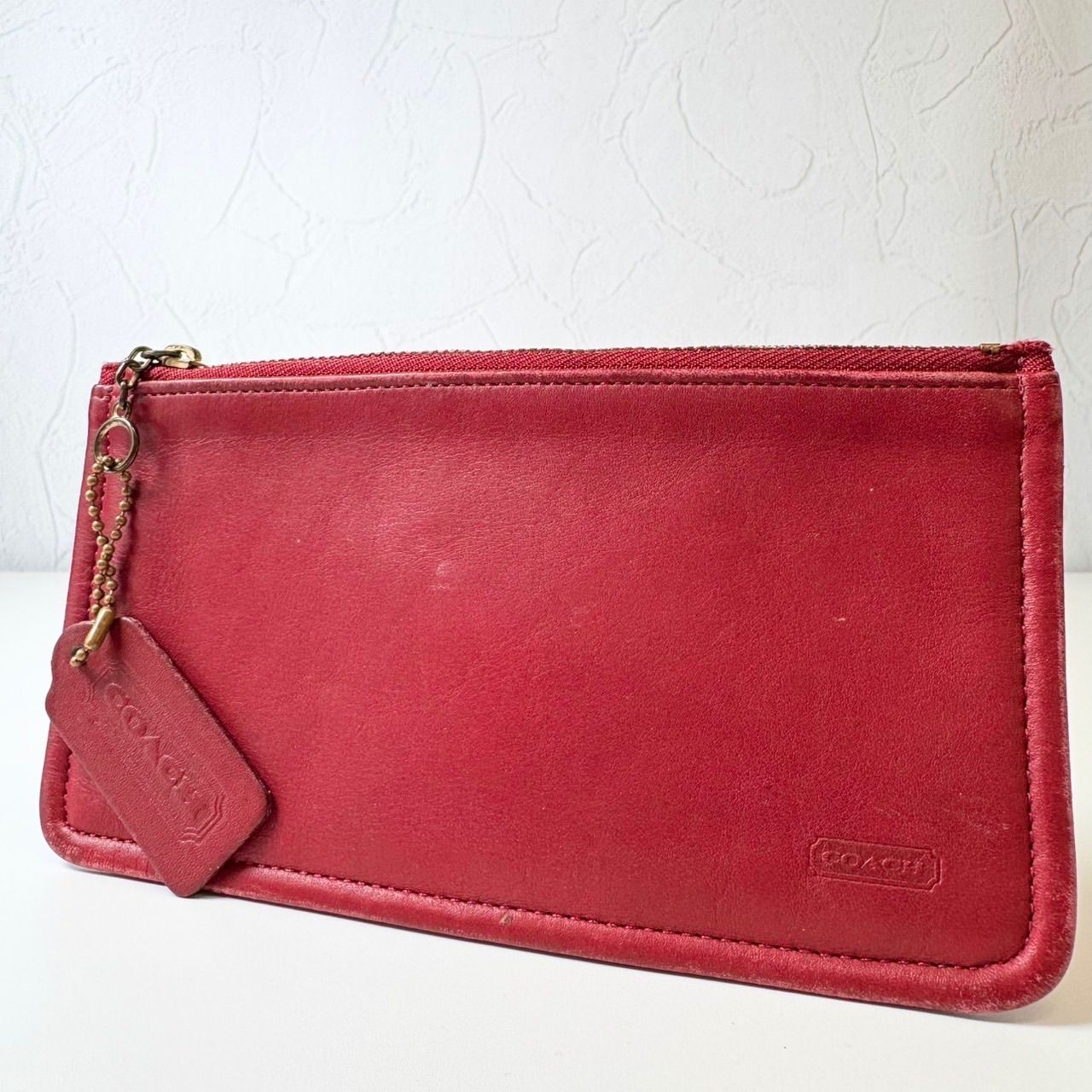Front view of a red Coach leather wallet pouch with a zipper and attached leather tag.
