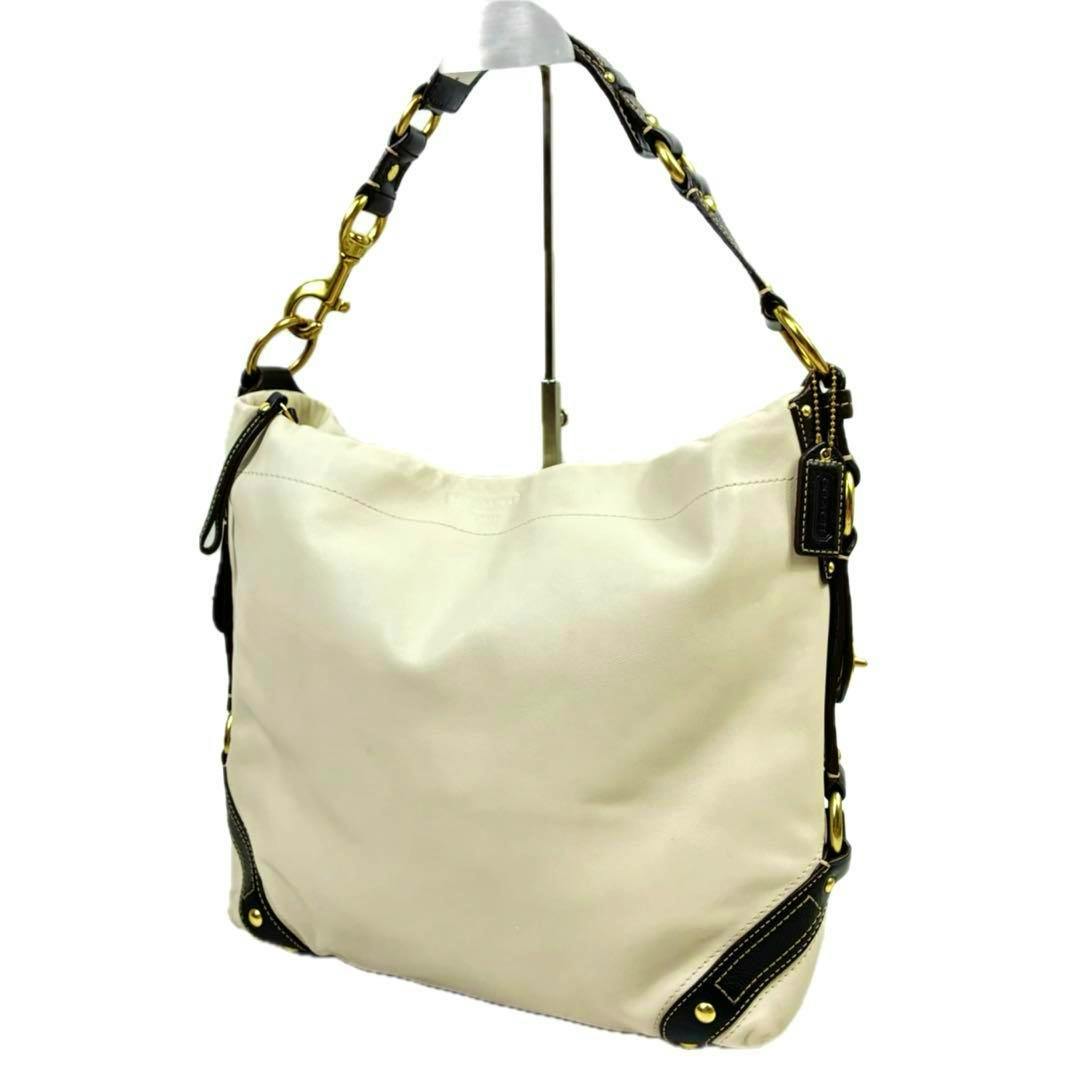 Off-white bicolor COACH one-shoulder bag (cow leather) with dark brown trim and gold hardware hanging on a display stand.