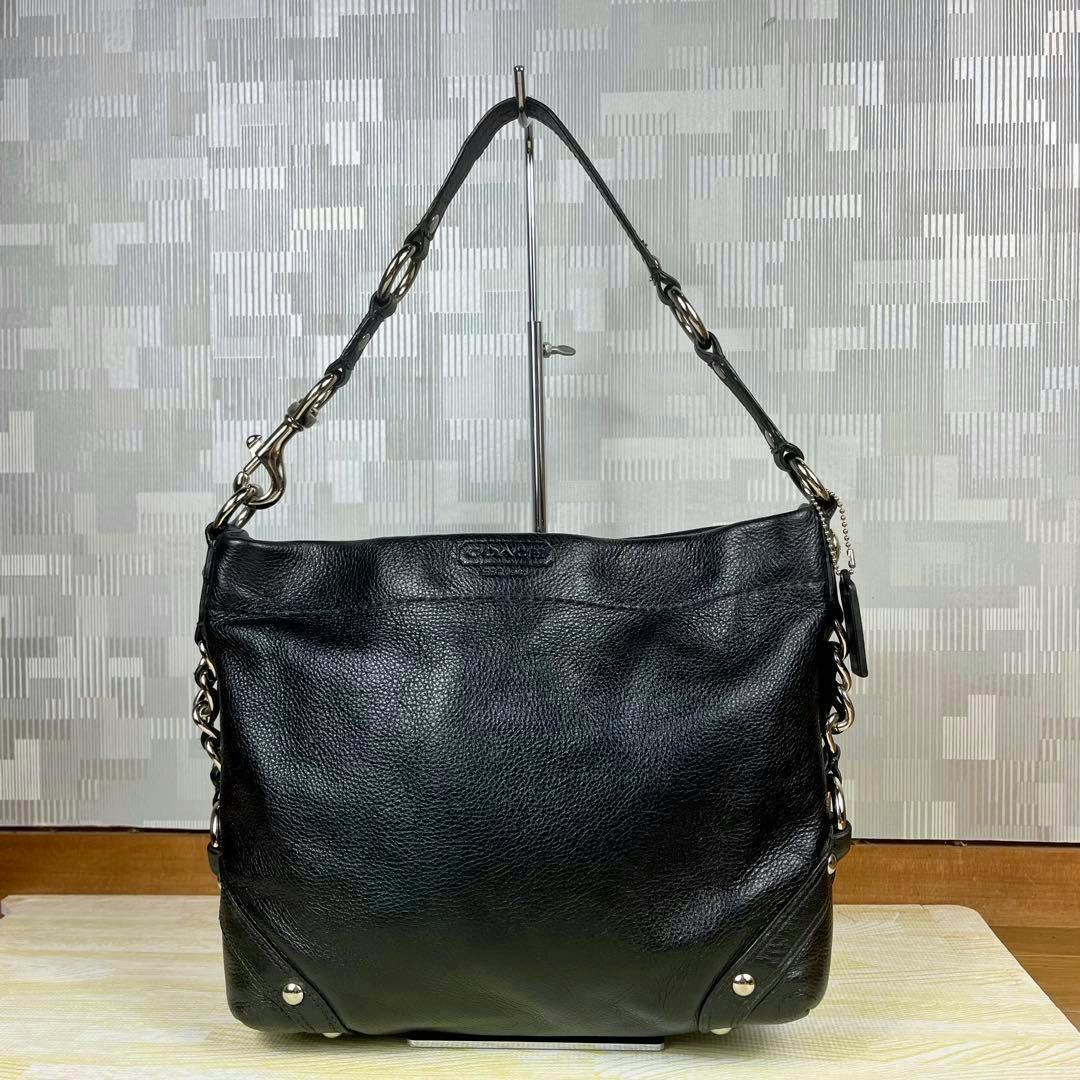 Front view of a black Coach one-shoulder bag hanging on a stand.