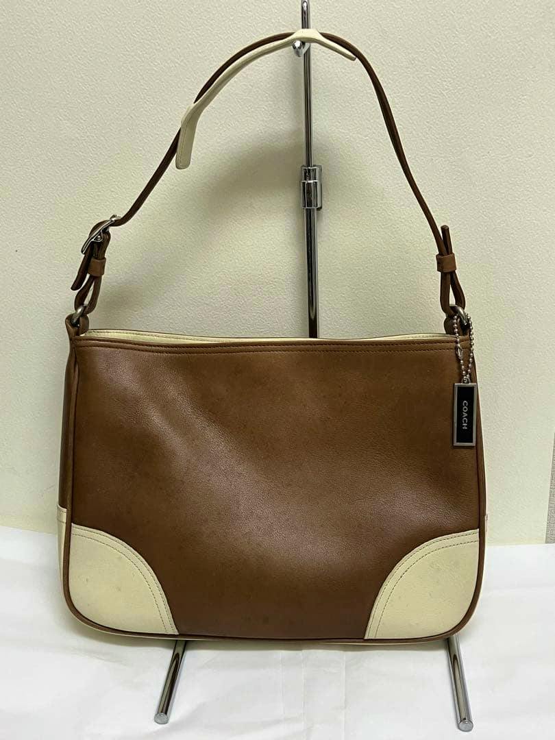 Front view of a brown and cream Coach one-shoulder bag on a display stand with a Coach hang tag.