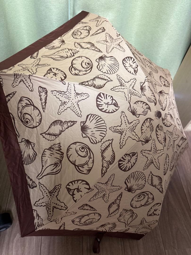 Open brown folding umbrella with seashell and starfish print visible on the canopy.