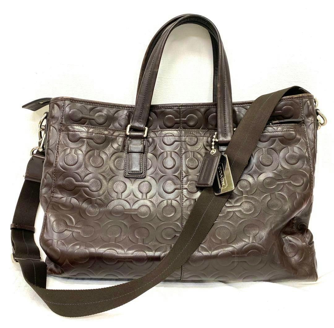 Dark brown COACH Op Art 2-way business bag with embossed circular pattern, twin top handles and a detachable shoulder strap shown front-on.