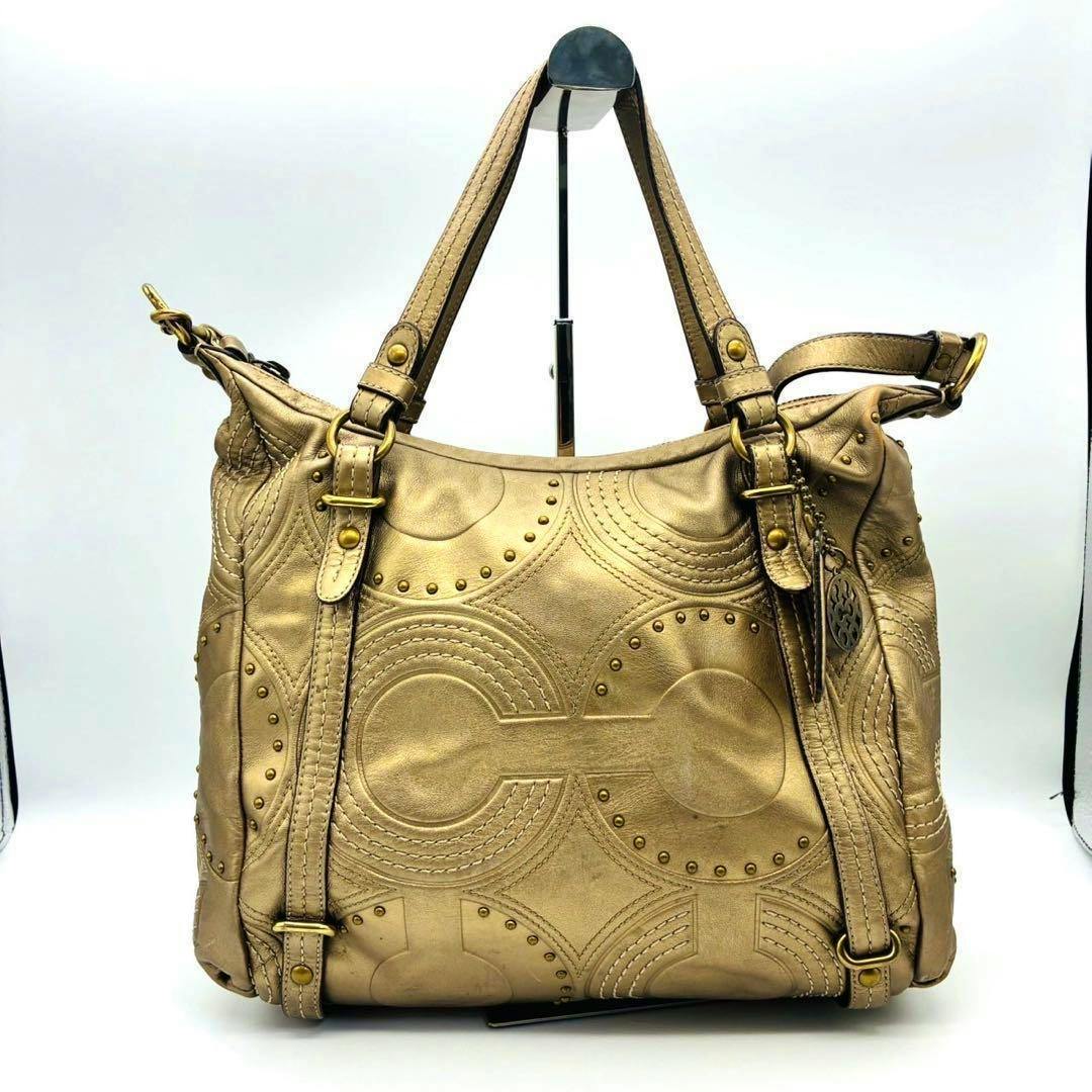 Gold leather COACH Op Art 2-way bag showing circular stitched pattern, gold studs, top handles, and a hanging Coach tag.