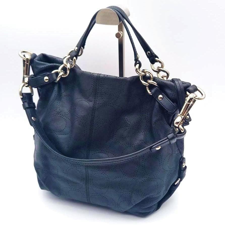 Black COACH Op Art Punching 2WAY bag on a stand showing perforated op-art pattern and gold-tone hardware.