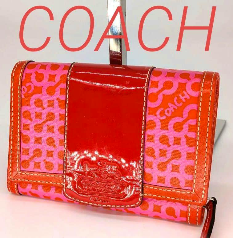 Front view of the COACH pink-orange op-art canvas tri-fold wallet with a red patent leather center strap and embossed logo.