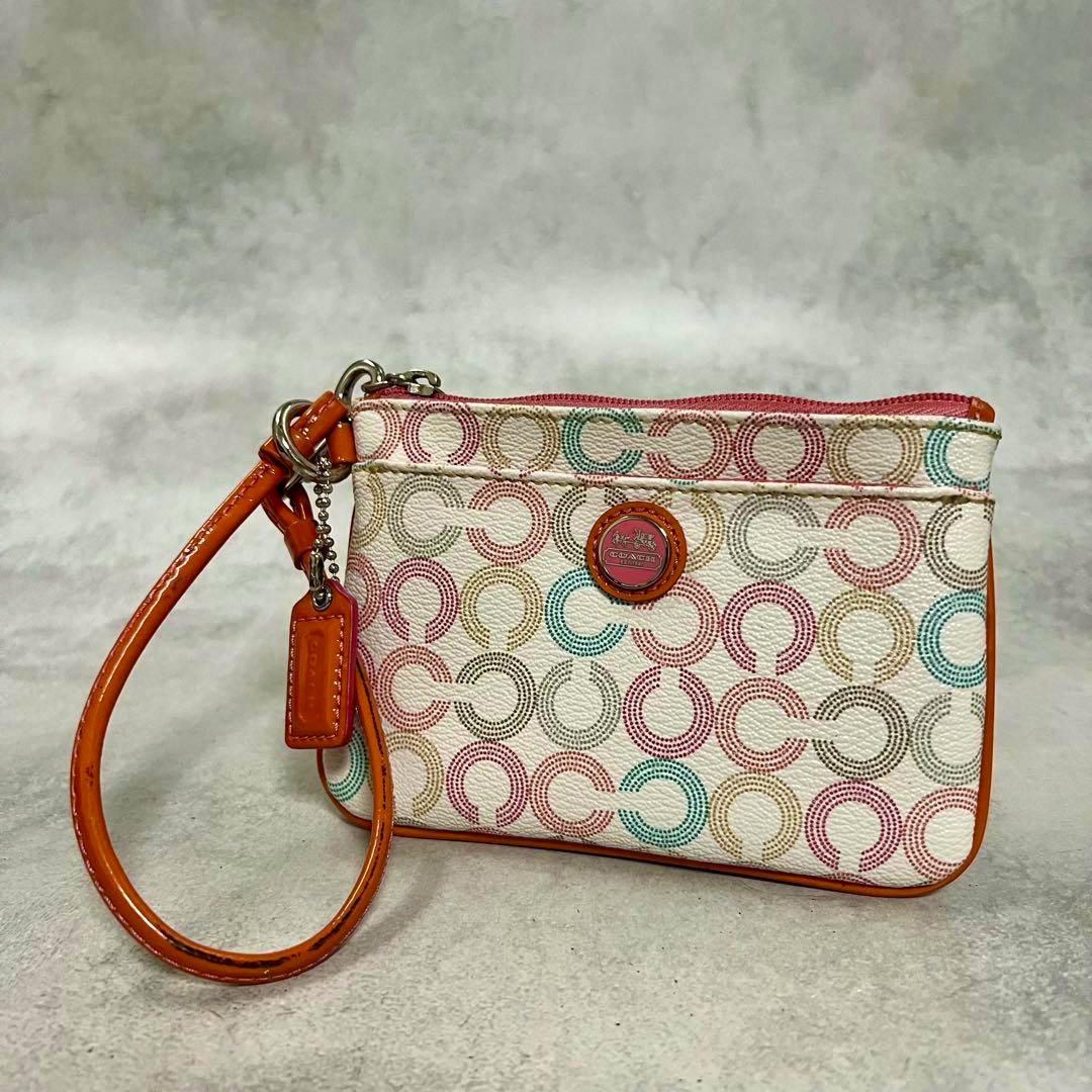 Front view of a COACH women's cow leather pouch with multicolored op-art C pattern, orange wrist strap, and round logo badge.
