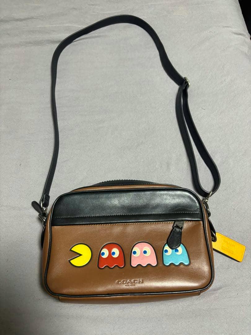 Front view of a COACH brown and black cow leather Pac-Man shoulder bag showing Pac‑Man and three ghost appliqués on the front and an adjustable strap.