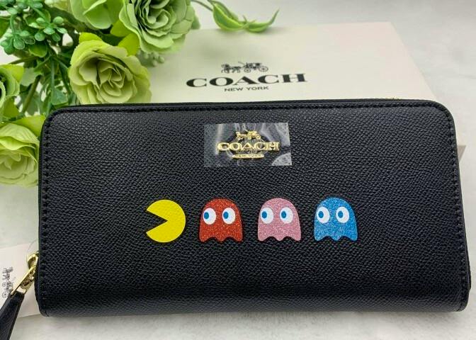 Front view of a black COACH long zip wallet on textured cow leather with Pac‑Man and ghost motifs.