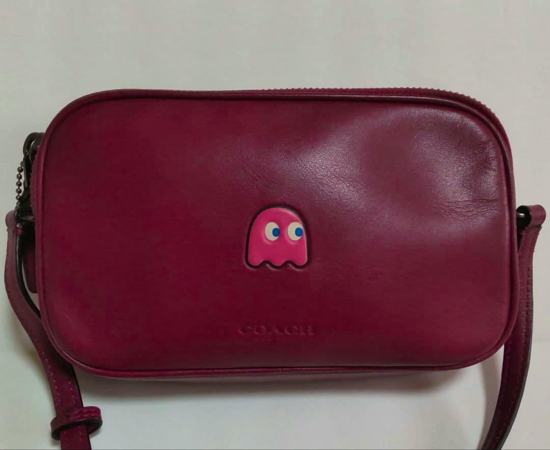 Front view of the COACH PACKMAN cow leather shoulder bag showing the bag front, a small ghost appliqué, and the attached shoulder strap.