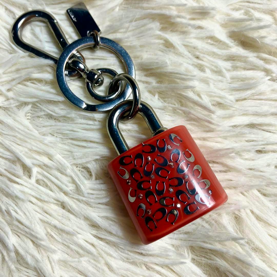 Red COACH padlock keychain with silver rings and clasp shown on a light fluffy background.