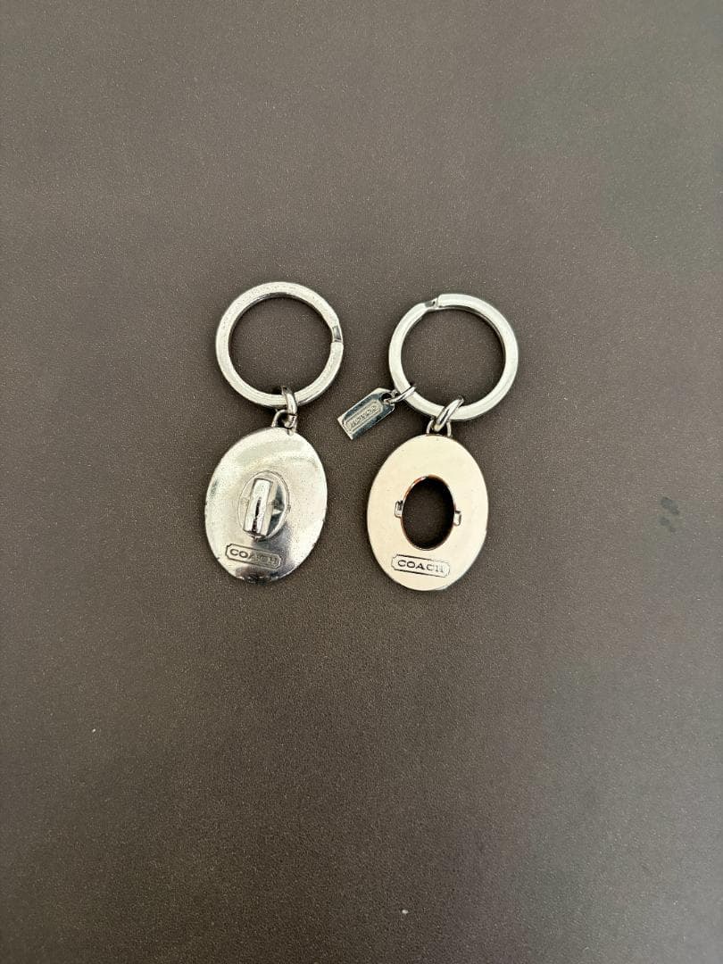 Two silver COACH key rings displayed flat on a dark background.