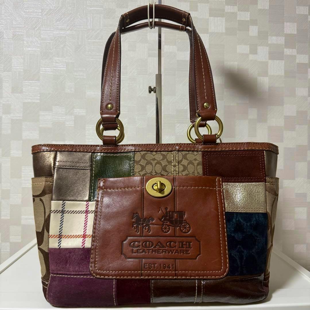 Front view of a Coach patchwork suede and leather tote bag with a turn‑lock pocket and top handles.