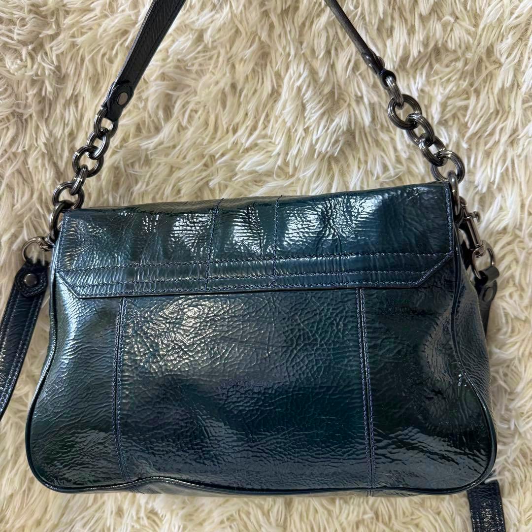 Back view of a navy patent leather COACH 2-way shoulder handbag lying on a light fur surface.