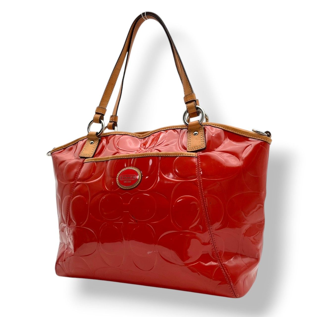 Red-orange Coach patent leather tote bag with embossed 'C' pattern and brown shoulder straps.