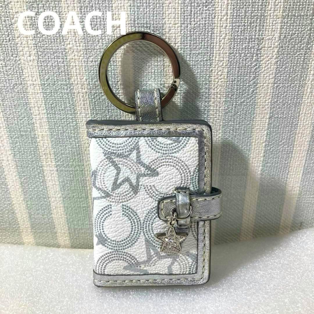 A Coach picture-frame keychain charm made of patterned leather with silver trim, attached to a metal key ring and a small star charm.
