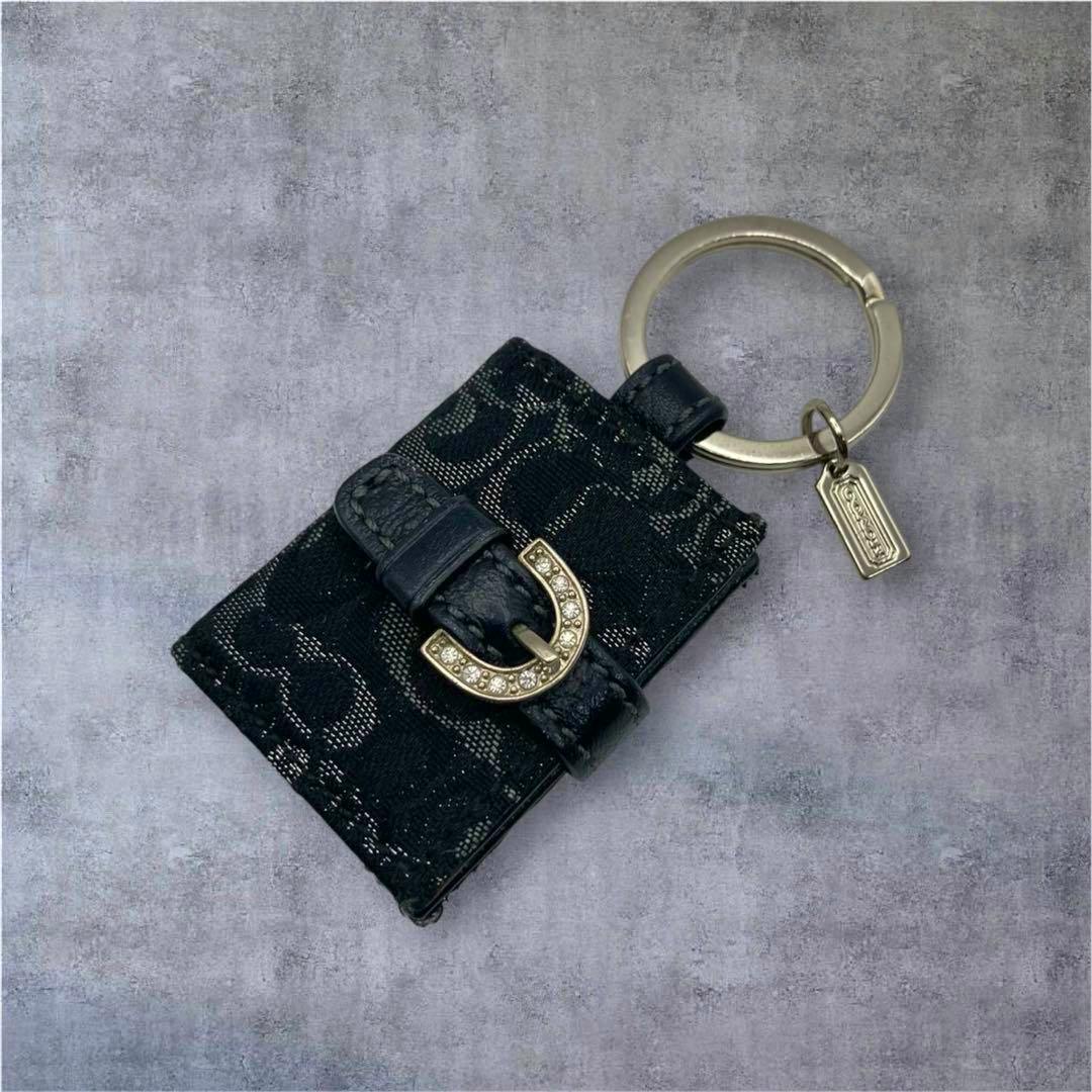Black COACH picture-frame key charm with signature patterned fabric, a rhinestone-studded gold buckle, and a metal key ring with a small Coach tag.